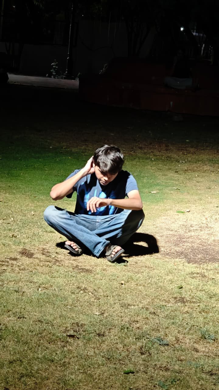 Chaitanya sitting cross-legged on grass at night